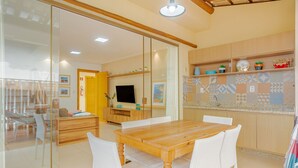 Una cocina moderna con una mesa de comedor de madera y sillas blancas, un televisor y una encimera con elementos decorativos.