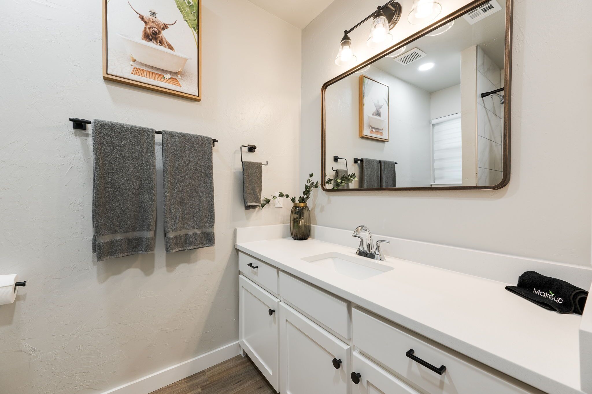 A bathroom with a white vanity, a large mirror, and two towels hanging on a rack.