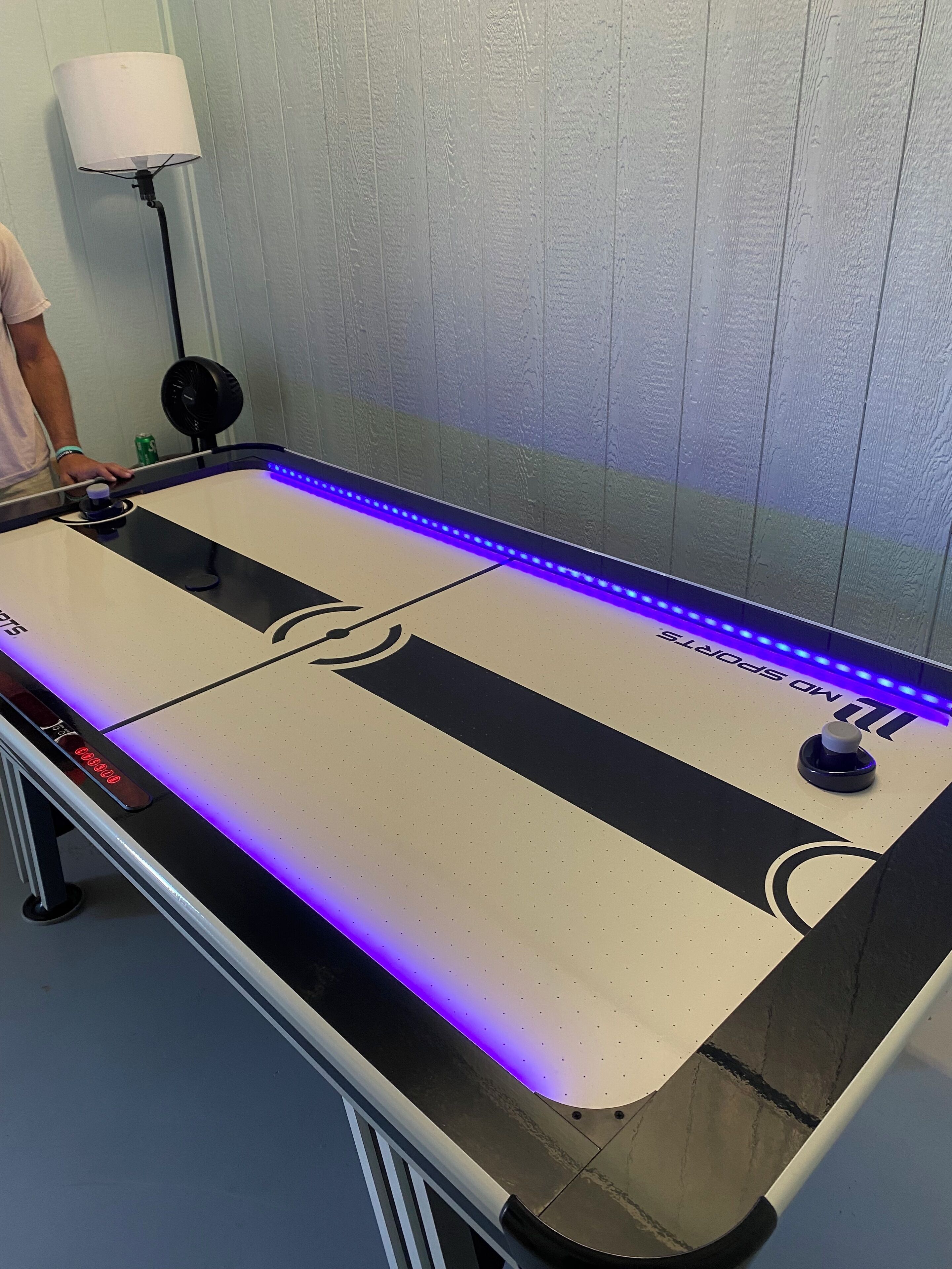 Une table dont le plateau est noir et blanc, avec des lumières LED bleues le long du bord, et un logo sur lequel on peut lire « PAS DE SPORTS ».