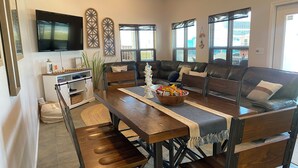 Un salón moderno con una mesa de comedor de madera oscura, sofá de cuero y un televisor montado en la pared.