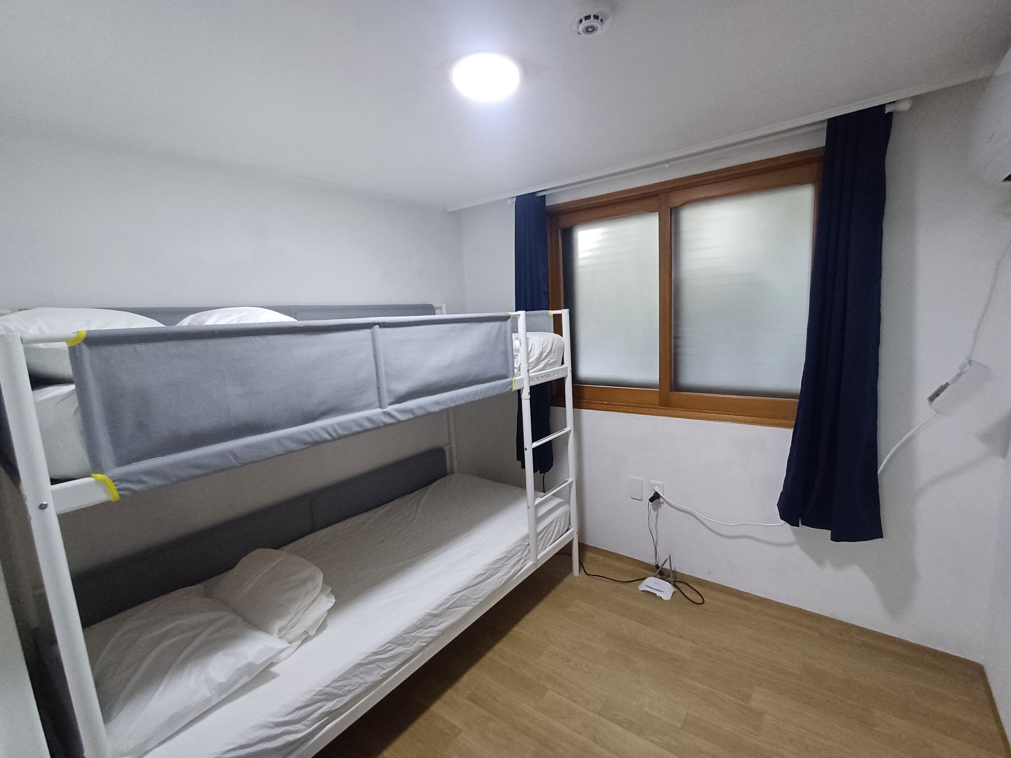 A bunk bed room with a window, a power outlet, and a wooden floor.
