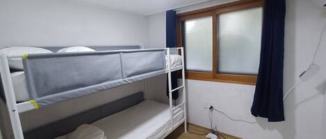 A bunk bed room with a window, a power outlet, and a wooden floor.