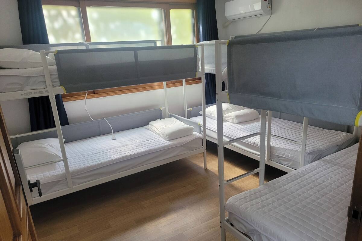 A bunk bed room with white bedding, a wooden floor, and a window with curtains.