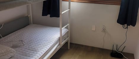 A small, well-lit room with a bunk bed, a window with curtains, and a wooden floor.