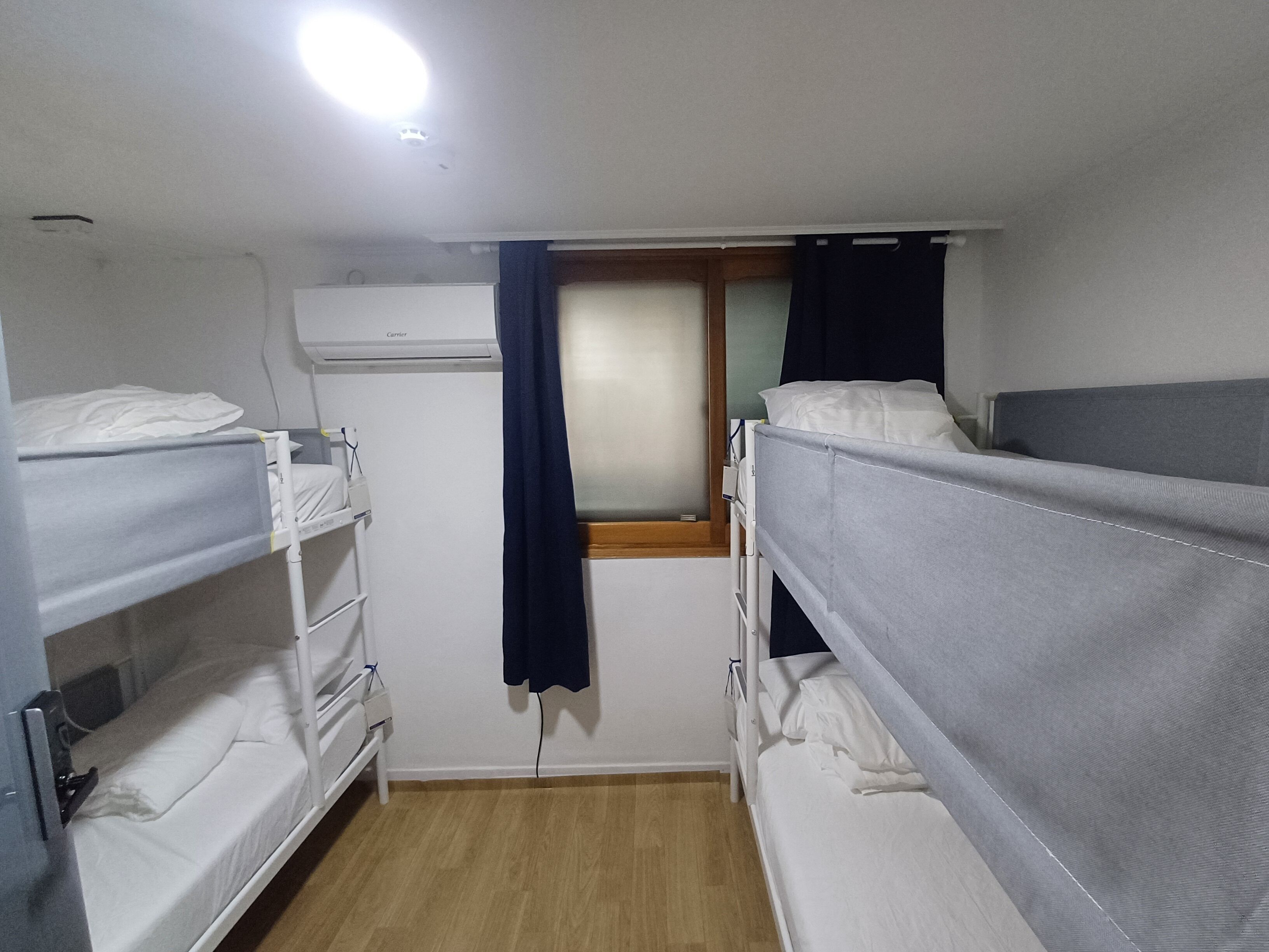A bunk room with two bunk beds, a window with curtains, an air conditioning unit, and a wooden floor.