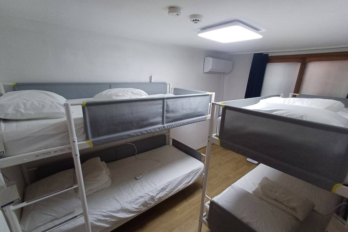 A dormitory room with bunk beds, a ceiling light, and an air conditioning unit.