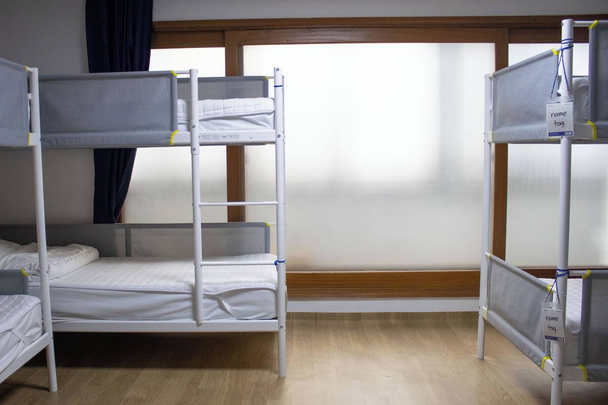 A bunk bed room with a window, wooden floor, and a curtain.