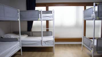 A bunk bed room with a window, wooden floor, and a curtain.