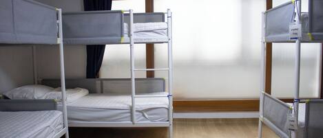 A bunk bed room with a window, wooden floor, and a curtain.