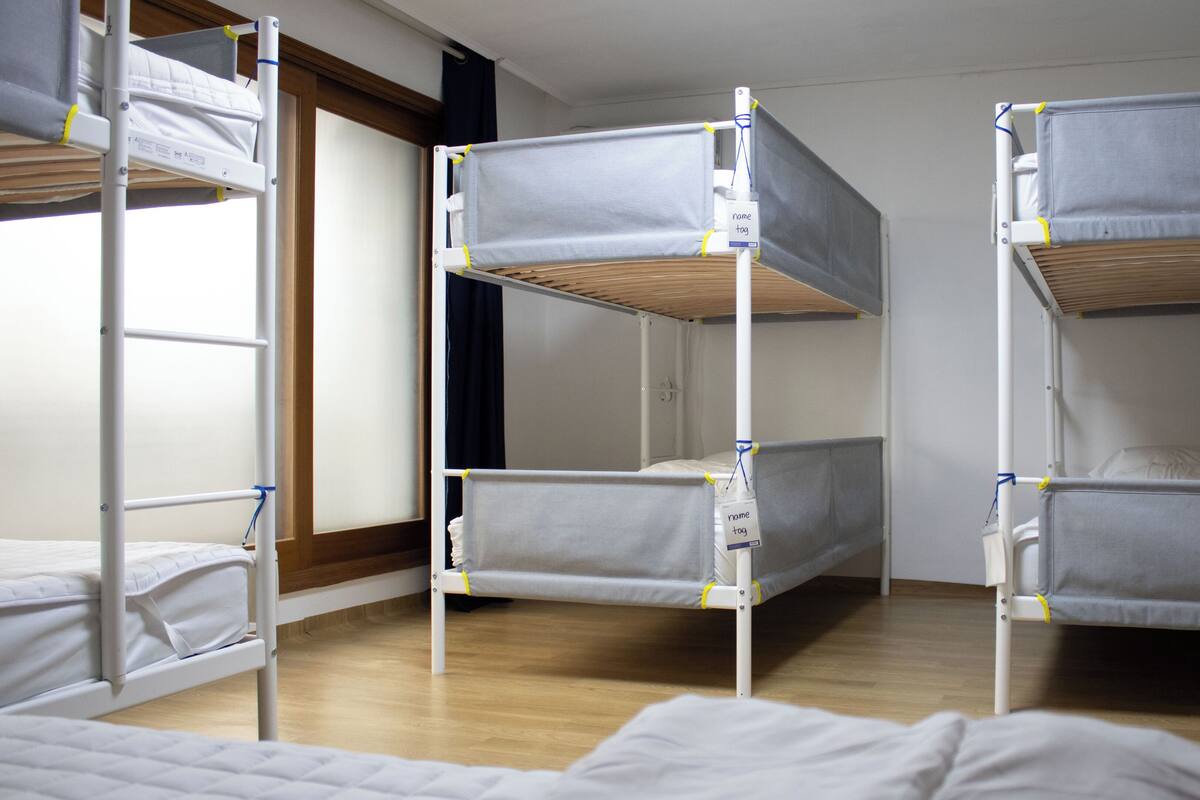 A room with bunk beds, wooden flooring, and a window with curtains.