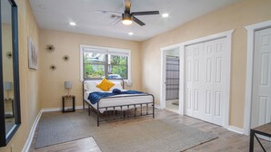 A bedroom with a bed, a ceiling fan, a window, and a door.