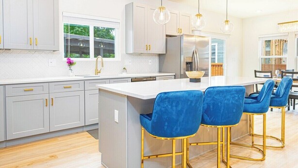A modern kitchen with grey cabinets, a white island, and blue bar stools.