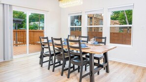 A dining area with a wooden table and chairs, large windows, and a view of a deck.