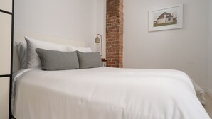 A neatly made bed with white bedding and two pillows, a brick wall, and a framed picture on the wall. - Luxurious Castle Loft Apartment in Montreal (Montreal)