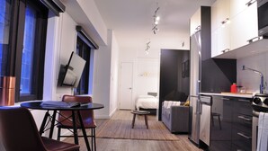 Eine moderne Küche mit Essbereich, einem kleinen Tisch und einer Couch. Im Hintergrund ist ein Bett zu sehen.