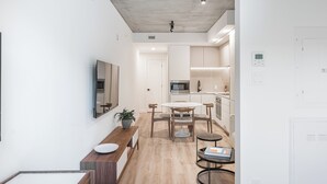 A modern kitchen with white cabinets, a microwave, and a sink. There is a dining area with a table and chairs, and a small round table with a book. - Modern Studio Haven in Le Mont (Montreal)