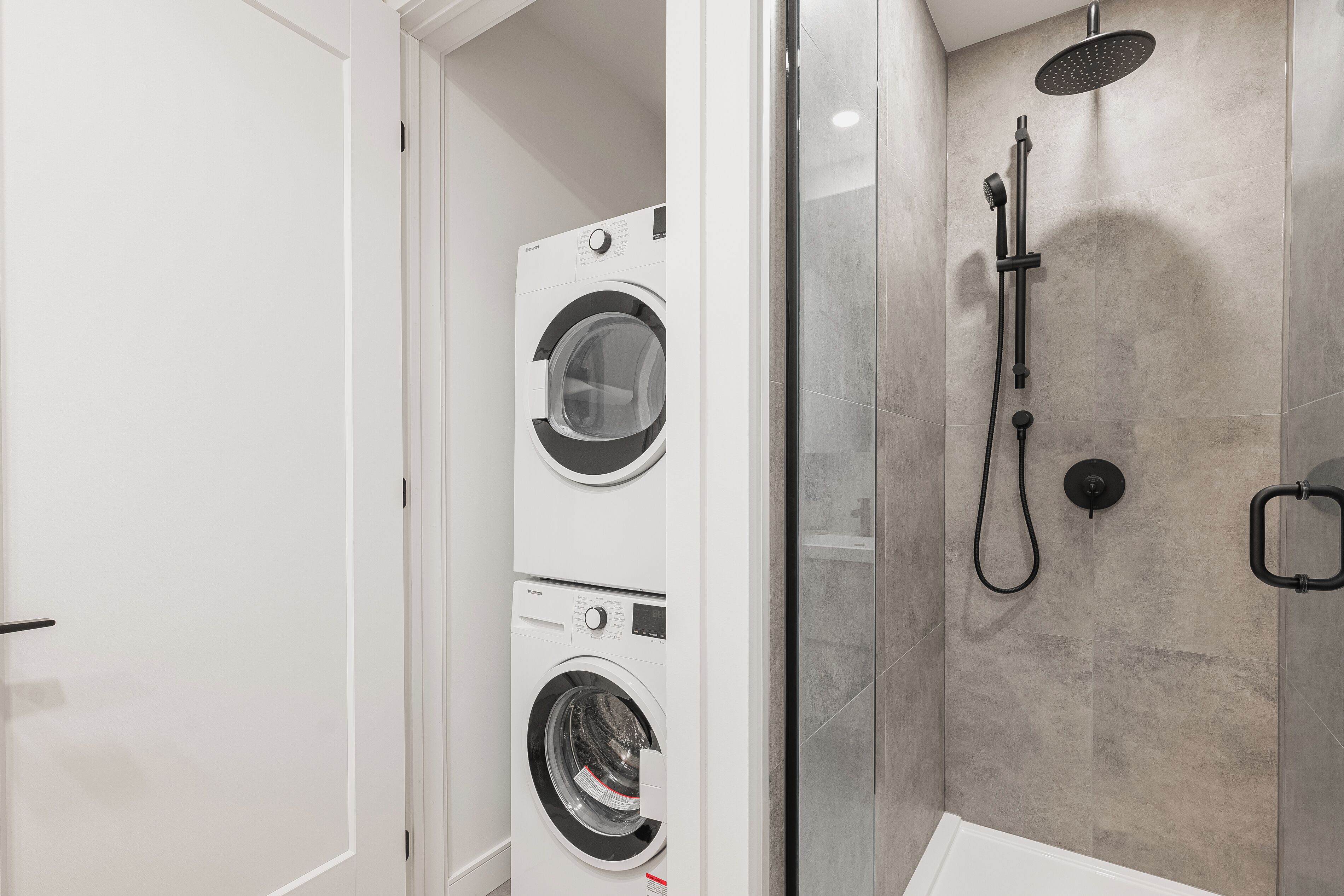 A modern bathroom with a built-in washer and dryer, a glass-enclosed shower, and a white bathtub.