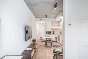 A modern kitchen with white cabinets, a microwave, and a sink. There is a dining area with a table and chairs, and a small round table with a book. - Experience Montreal Living at Le Mont (Montreal)