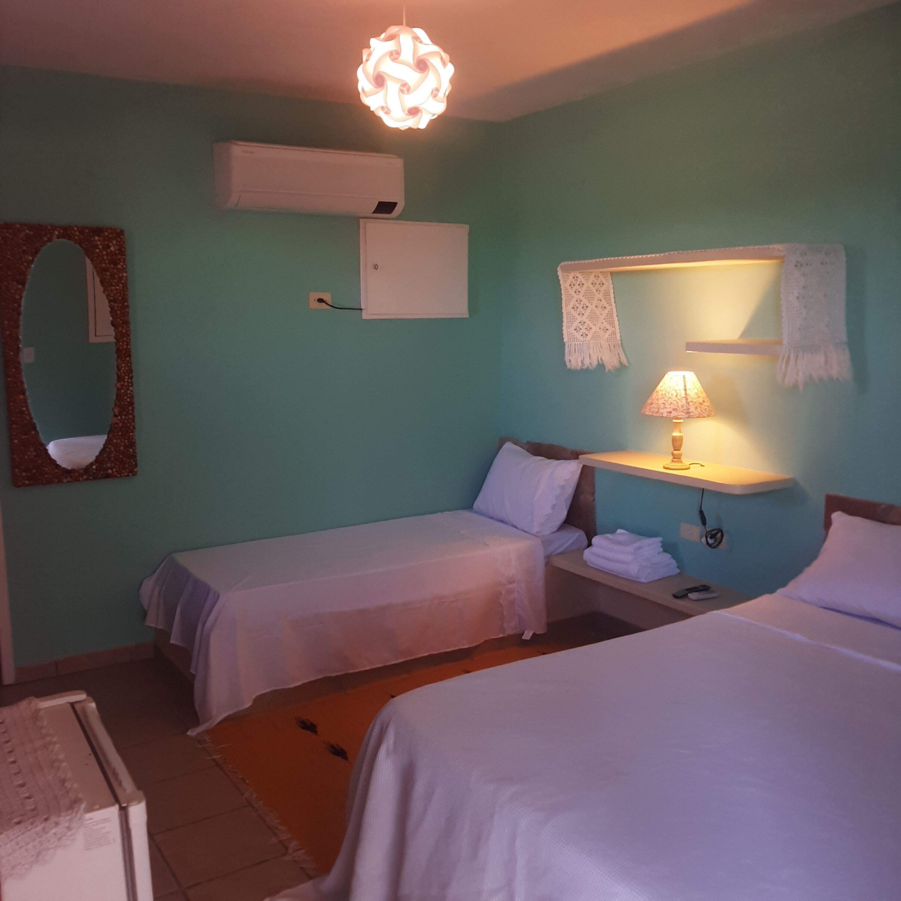 Une chambre avec deux lits simples, une table de chevet avec une lampe, un climatiseur mural et un miroir décoratif.