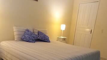 Un dormitorio con cama, mesita de noche, lámpara, una puerta y un cuadro en la pared.