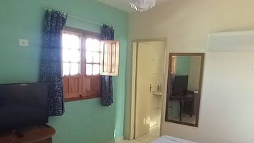 A bedroom with a bed, a television on a wooden table, a window with curtains, and a door.