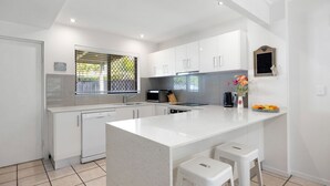 A modern kitchen with white cabinetry, a central island, and bar stools. - Cassindah 7 Noosaville (Noosaville)
