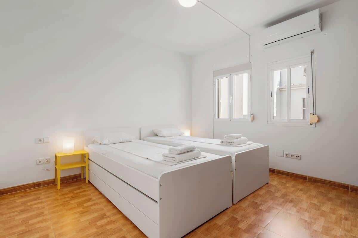 Quarto limpo e moderno com duas camas de solteiro, uma pequena mesa de cabeceira, um espelho e uma janela.