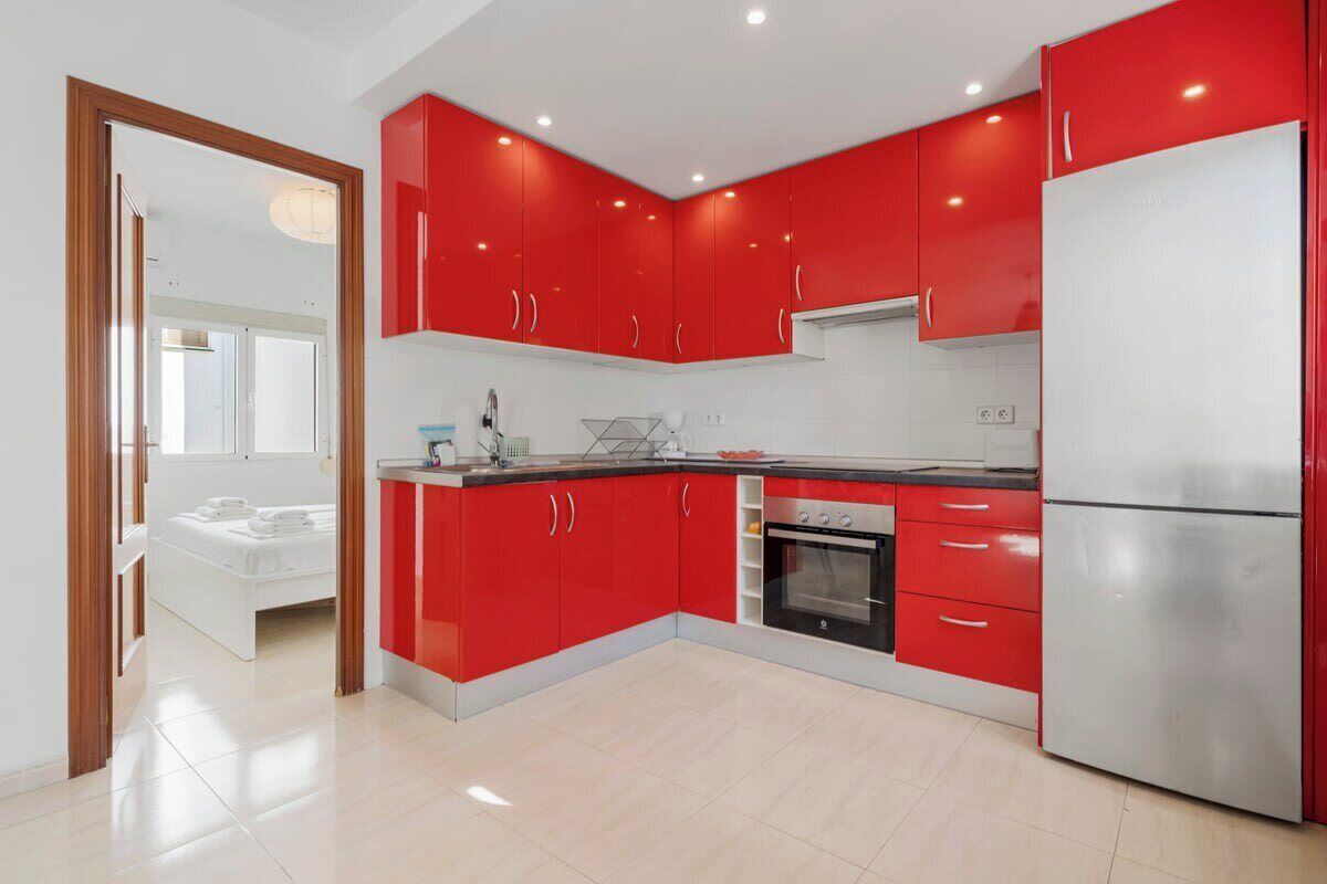 A modern kitchen with red cabinets, a stainless steel refrigerator, and a built-in oven.