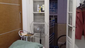 Et lille soveværelse med en seng, en stol, en ventilator og en cykel i baggrunden.