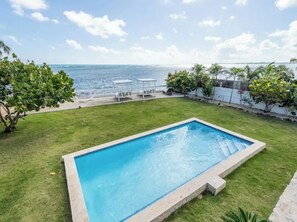 A rectangular swimming pool with a clear blue water surface, surrounded by a well-maintained lawn and a white fence.