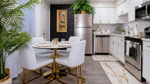Una cocina moderna con armarios blancos, electrodomésticos de acero inoxidable y un comedor con mesa redonda y sillas blancas.