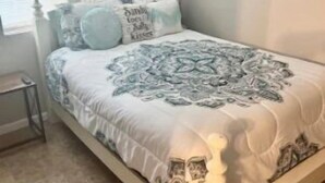 Un dormitorio con cama, ventilador de techo, ventana con persianas y mesita de noche.