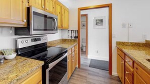 A kitchen with wooden cabinets, a microwave, a stove, and granite countertops. - Condo With Mountain and Lake Views/Clubhouse Access (Keystone)