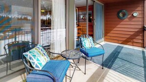 A covered outdoor seating area with two chairs and a small table, a sliding glass door, and a wooden wall with a clock and a mirror. - Condo With Mountain and Lake Views/Clubhouse Access (Keystone)