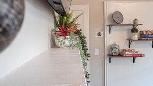 A hallway with a white bench, a potted plant, and shelves with board games and a small clock. - Marietta Square's Home Away! (Marietta)
