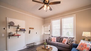 A living room with a dark wood floor, a ceiling fan, a sofa with floral cushions, and a coffee table. - Marietta Square's Home Away! (Marietta)
