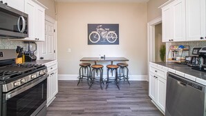 A kitchen with white cabinets, a stove, a dishwasher, and a bar area with stools. - Marietta Square's Home Away! (Marietta)