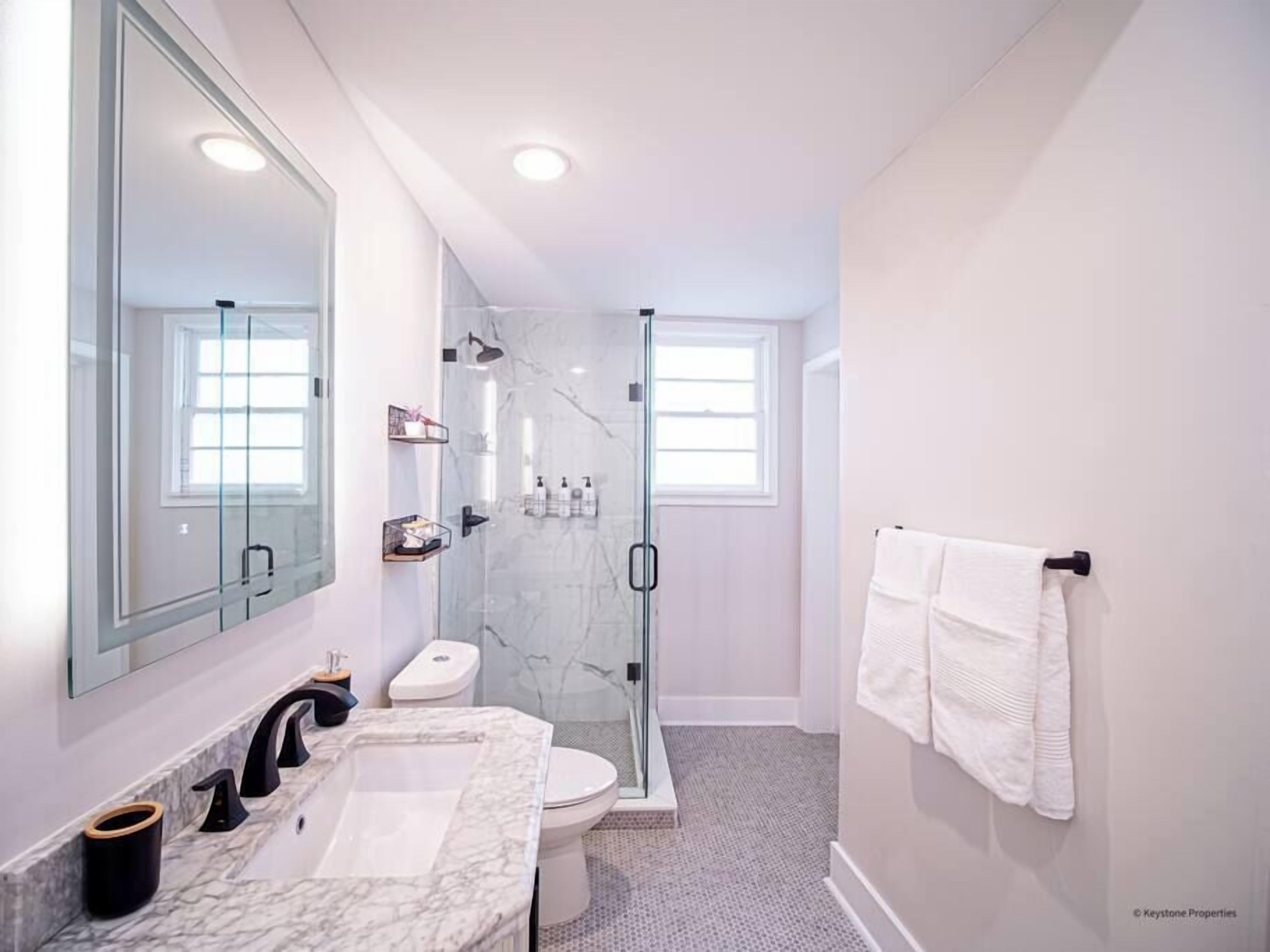 A modern bathroom with a glass-enclosed shower, a large mirror, and a marble sink.