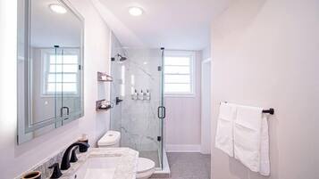 A modern bathroom with a glass-enclosed shower, a large mirror, and a marble sink.
