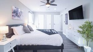 A modern bedroom with a bed, bedside tables, a ceiling fan, a TV, and a potted plant.