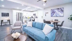 A modern living room with a blue sofa, a dining table, and a ceiling fan.