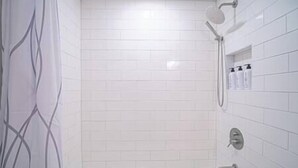 A bathroom with white tiled walls, a shower, and a bathtub. There are three bottles on the wall.