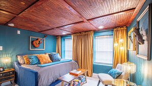 Een slaapkamer met een bed, bureau, stoel en een raam met gordijnen.