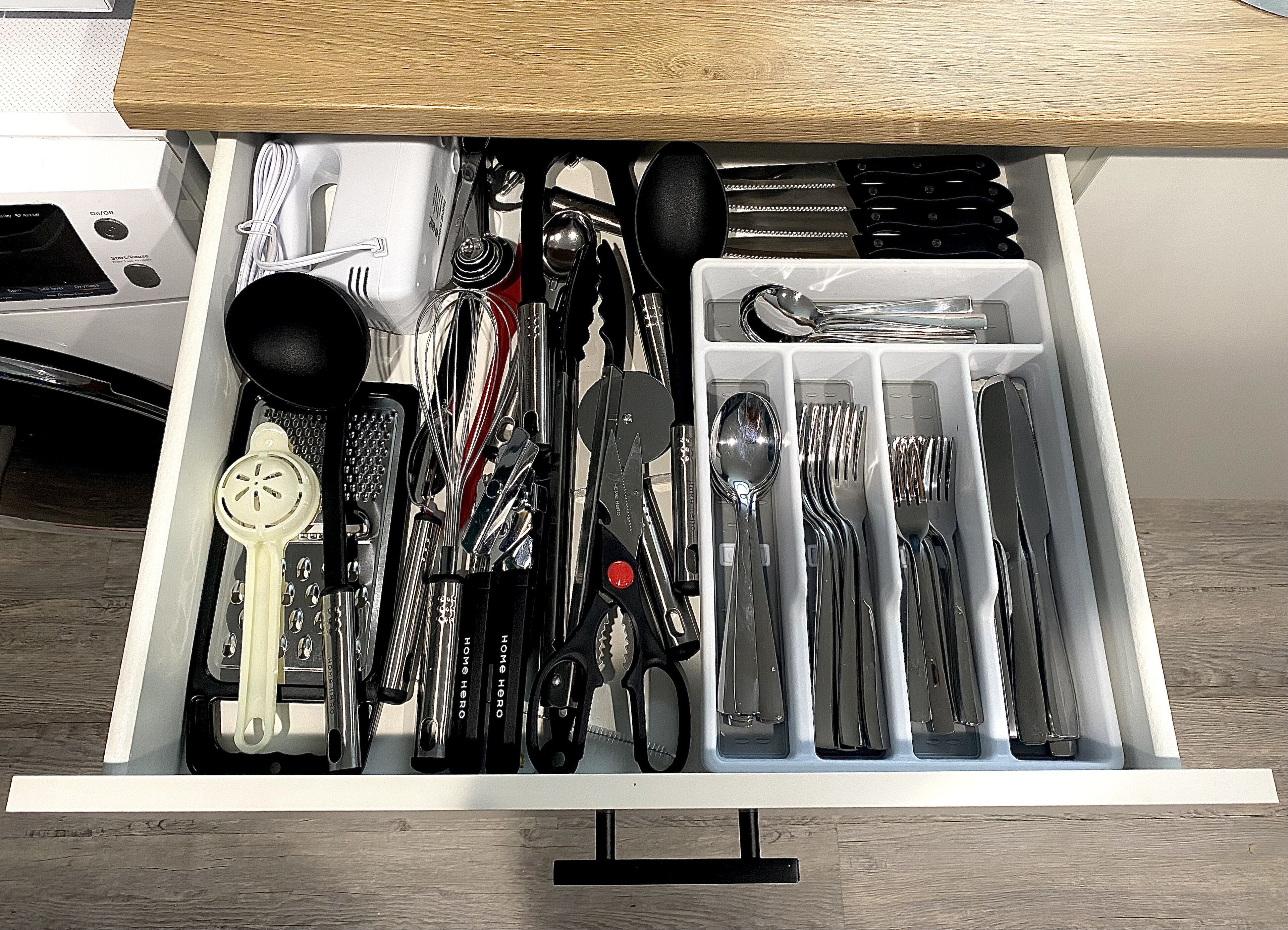A drawer with various kitchen utensils and tools, including knives, spoons, and a grater.