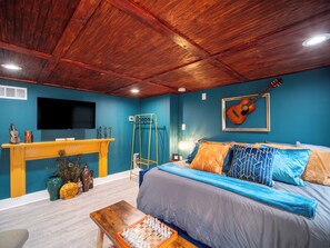 A bedroom with a wooden ceiling, a bed with blue and orange bedding, a TV on the wall, and a guitar. - Rhythmic Escape - Marietta Square! (Marietta)