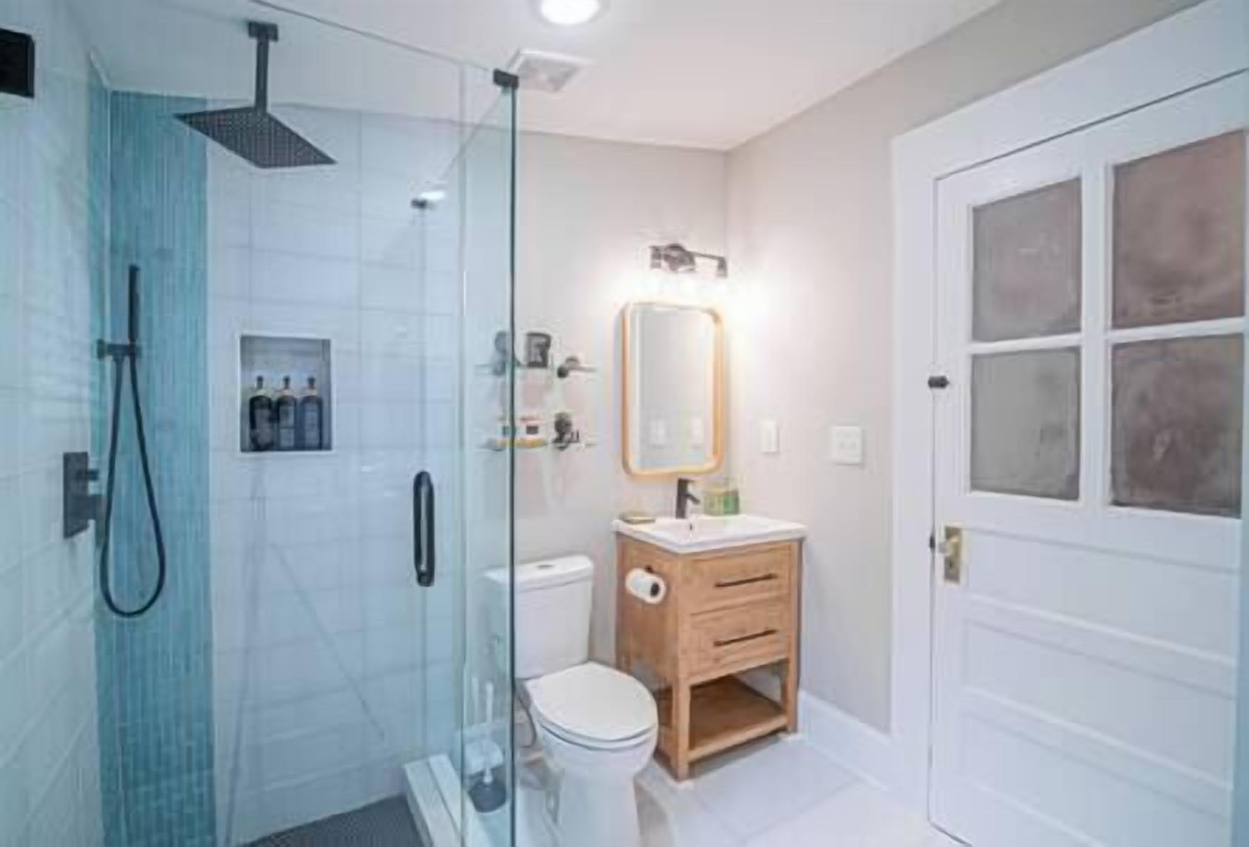 A modern bathroom with a glass-enclosed shower, a wooden vanity, and a white toilet.
