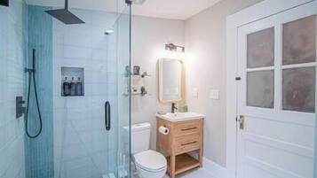A modern bathroom with a glass-enclosed shower, a wooden vanity, and a white toilet.