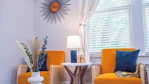 A room with two orange armchairs, a small white table, a lamp, and a decorative wall piece. - Lumiére of Marietta Square (Marietta)