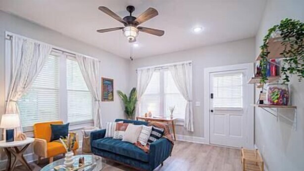 A living room with a blue sofa, a glass coffee table, and a ceiling fan. - Lumiére of Marietta Square (Marietta)