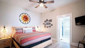 A bedroom with a wooden bed, a ceiling fan, a wall-mounted TV, and a door leading to another room. - Lumiére of Marietta Square (Marietta)